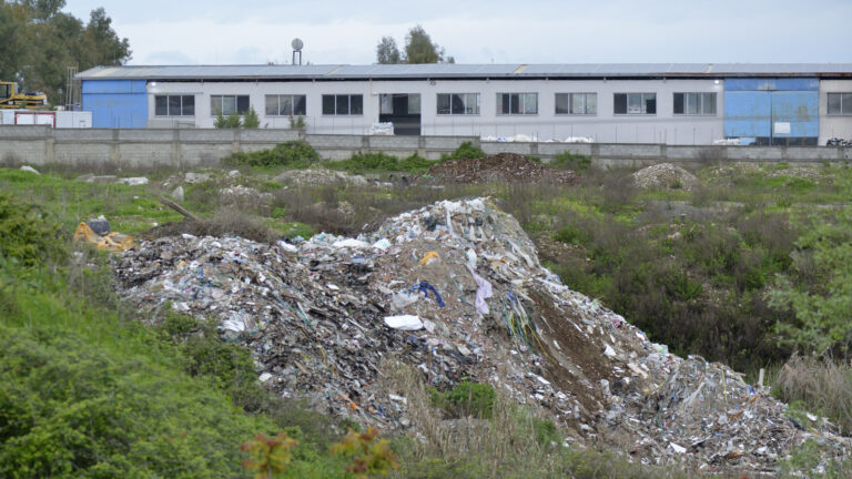 Mbetje urbane të hedhura në brigjet e Tërkuzës. Në sfond, një fabrikë prodhimi plastmasi. Kamëz. © Artan Rama.